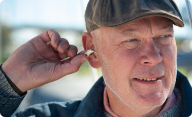 Äldre man som använder hörapparat i behov av Otinova öronspray.